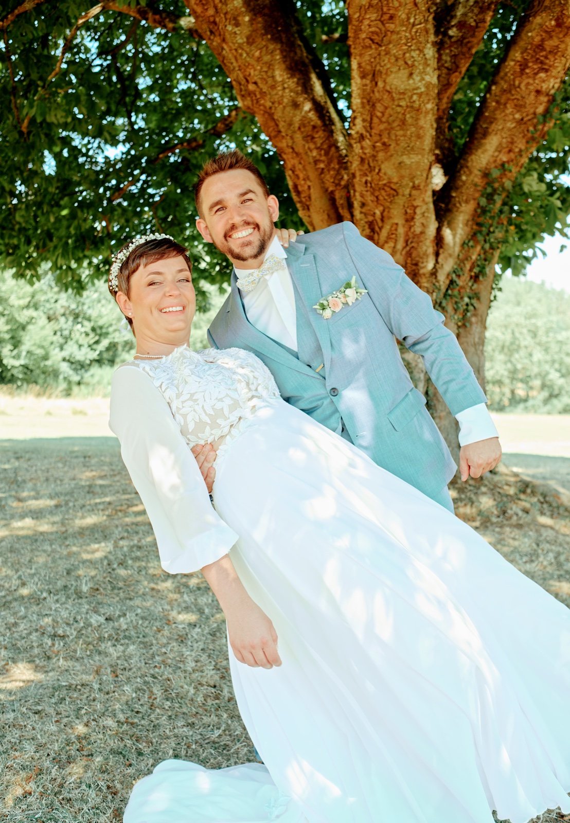 Couple de mariés souriant sous un grand arbre